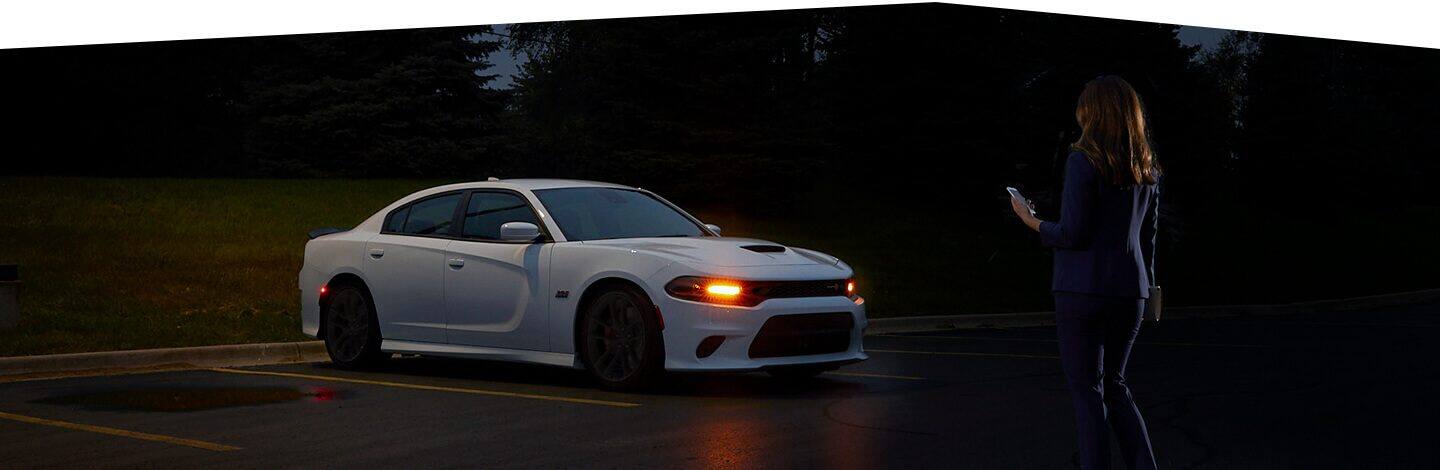 A woman approaching a 2020 Dodge Charger at night with its headlamps illuminated.