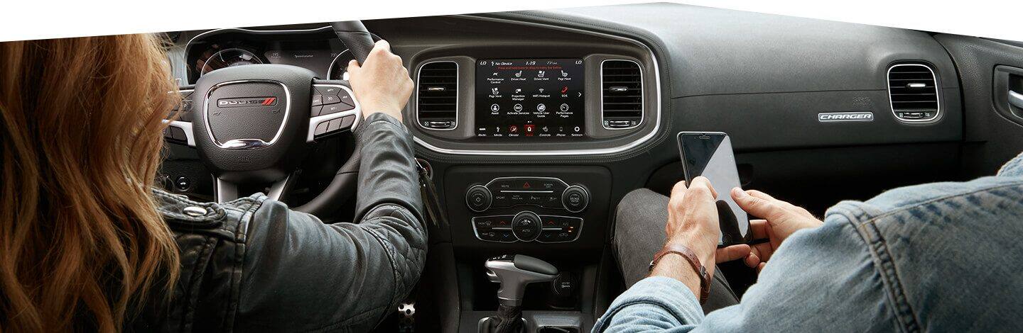 A driver with her hands on the wheel and a front seat passenger on his phone in the 2020 Dodge Charger.