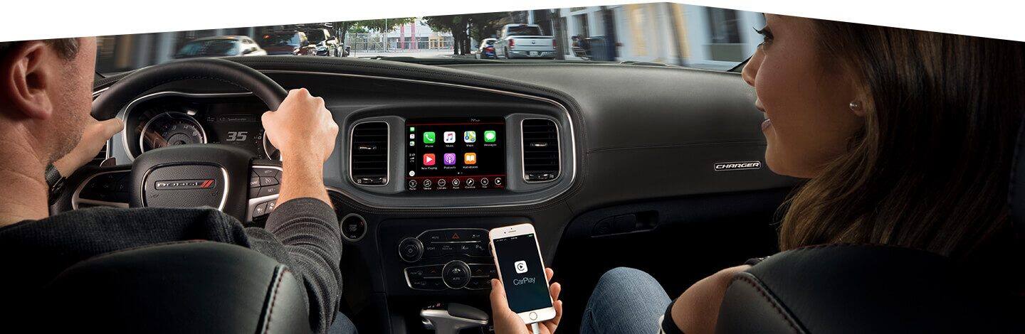The front passenger in the 2020 Dodge Charger holding a smartphone with Apple CarPlay on the touchscreen.