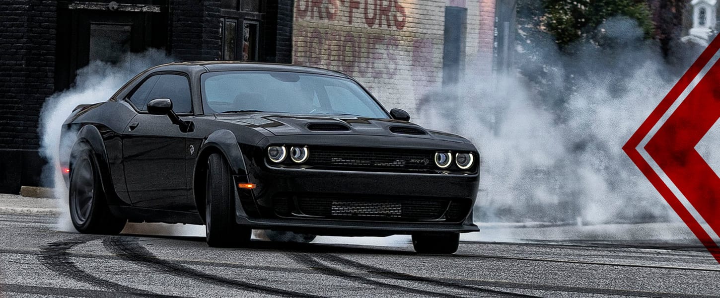 An angled front profile of a black 2023 Dodge Challenger SRT Hellcat taking a curve on a city street dusted with snow.