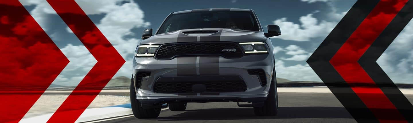 A head-on view of a gray 2023 Dodge Durango SRT Hellcat with dual dark gray center stripes, being driven on a track. 