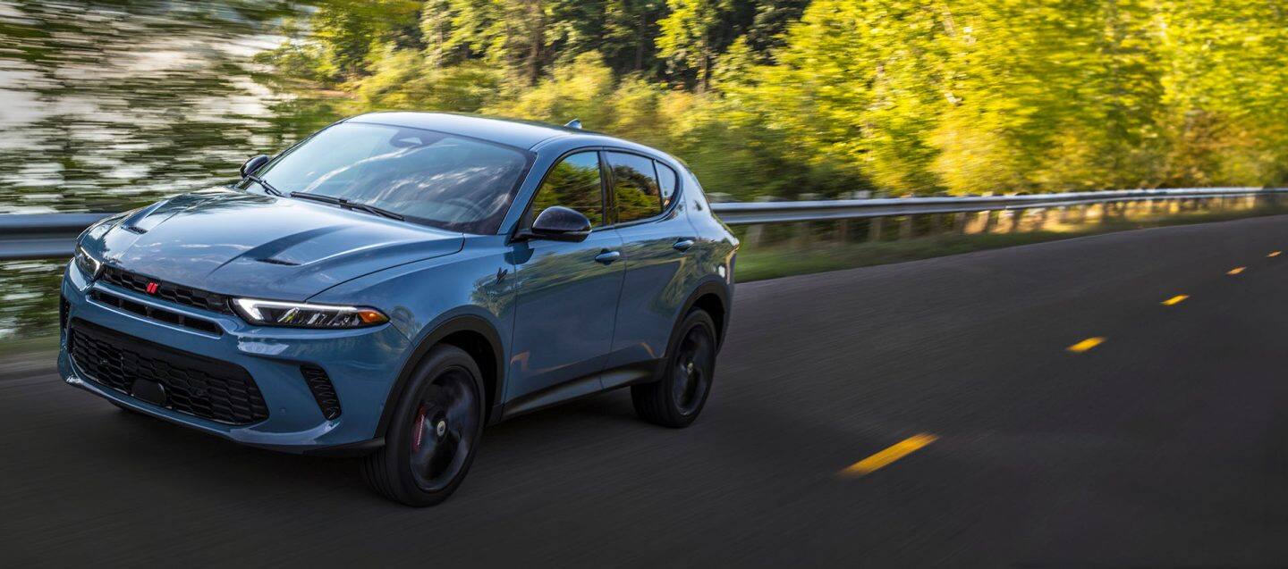 A front angled driver-side profile of a blue 2023 Dodge Hornet GT being driven on a highway, with the background blurred to indicate the vehicle is in motion.