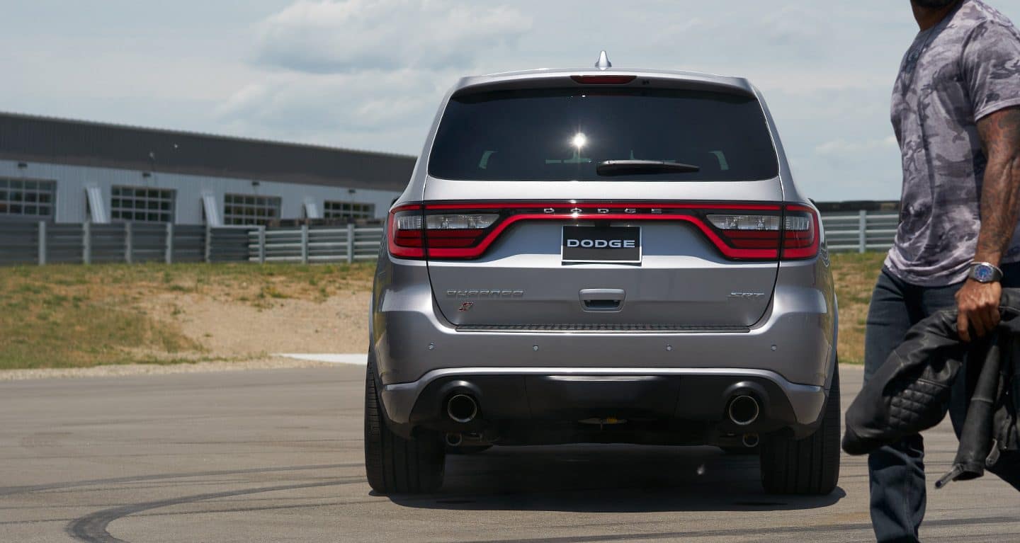 Display A man carrying a leather jacket approaching a 2020 Dodge Durango parked in an empty lot. 