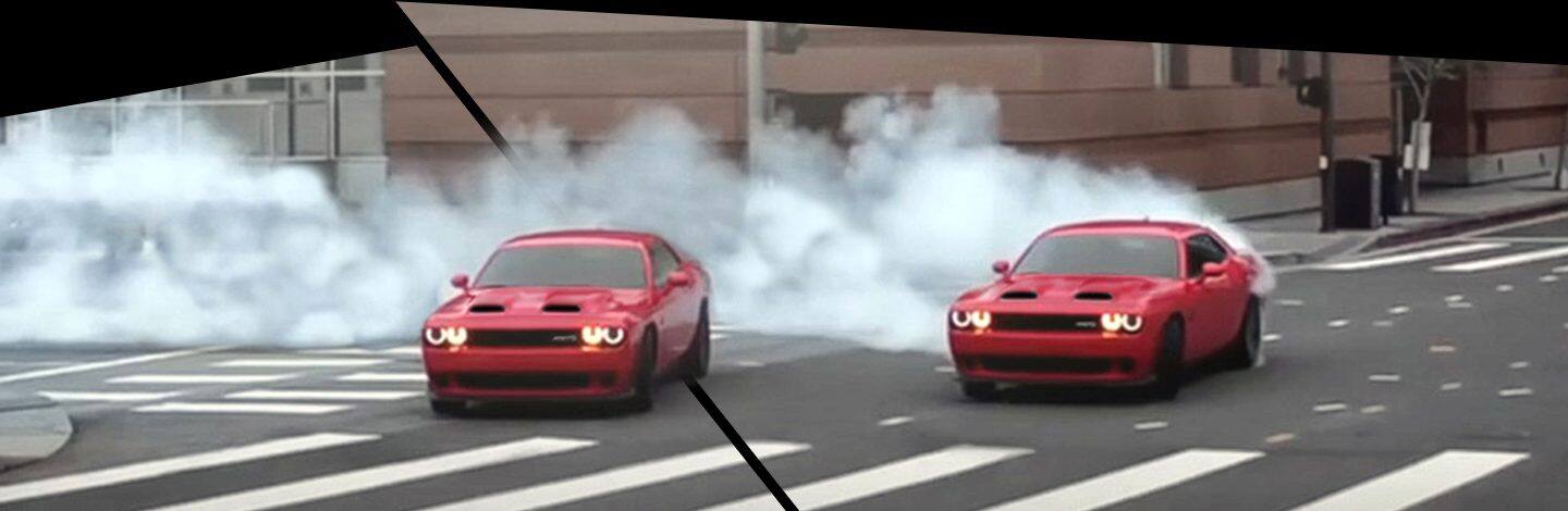 Two 2021 Dodge Challenger SRT Hellcat Redeye models making a sharp turn on a city street, smoke pouring from their rear tires.