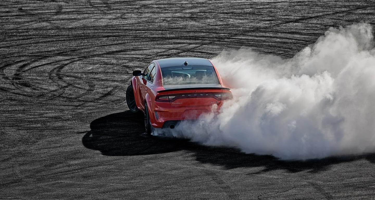A red 2021 Dodge Charger SRT Hellcat Redeye on blacktop, with smoke billowing from its tires.