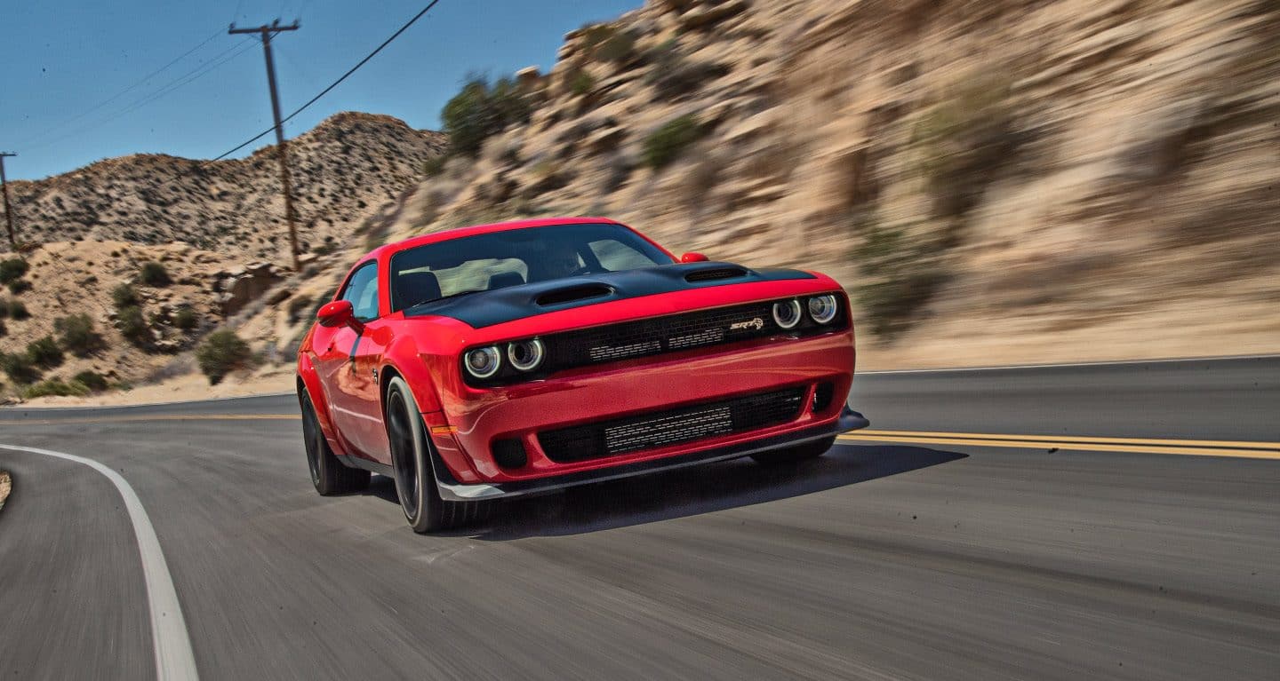 Display A red 2022 Dodge Challenger SRT Hellcat Redeye Widebody driving down a road with desert mountains to the right.