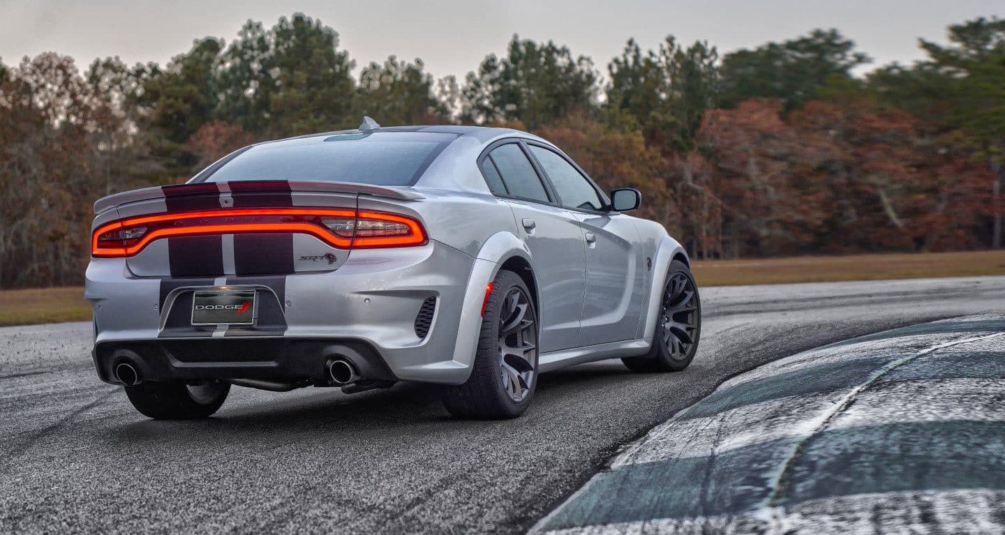 Display A rear view of a 2022 Dodge Charger SRT Hellcat Widebody taking a curve on a road.