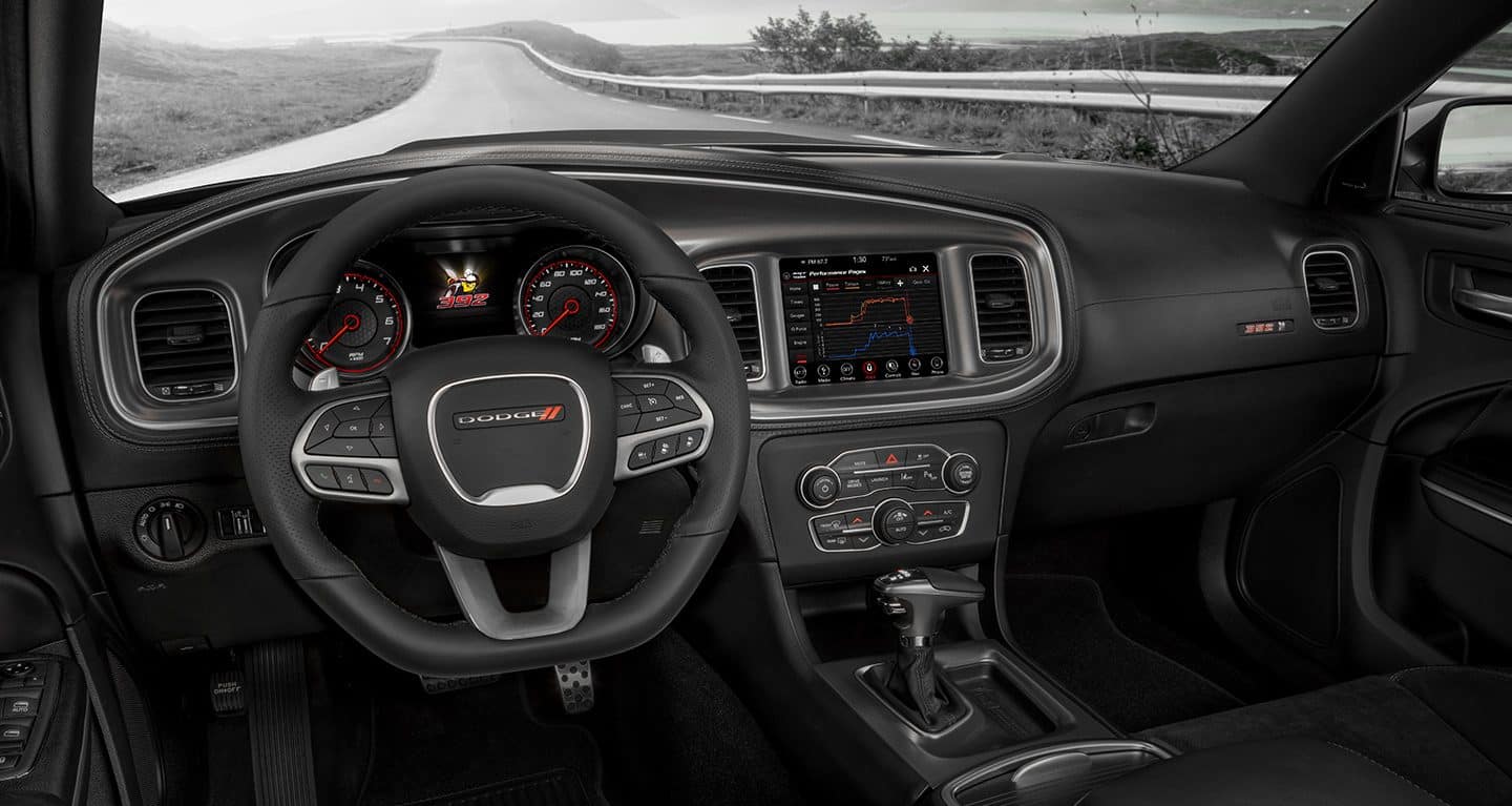 The interior of the 2022 Dodge Charger Scat Pack focusing on the steering wheel, instrument cluster, Uconnect touchscreen, center console and glove compartment.
