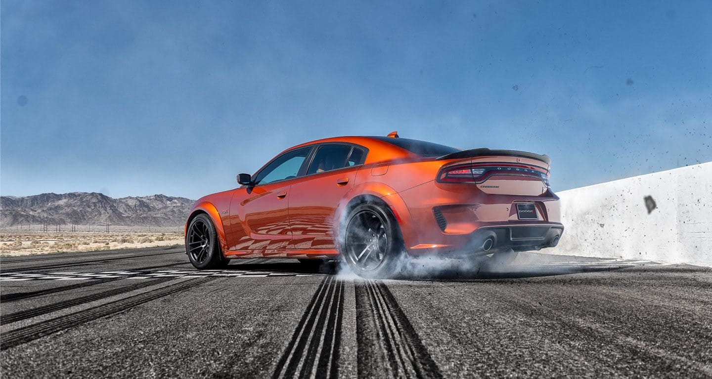 The 2022 Dodge Charger Scat Pack spinning its rear wheels on a track with dust rising from them.