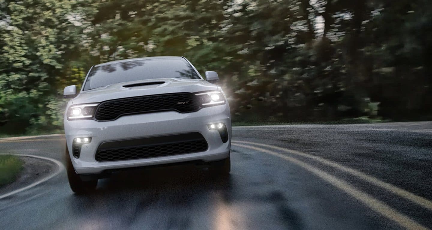 Display A head-on view of a white 2022 Dodge Durango Citadel with its headlamps on, taking a curve at speed.