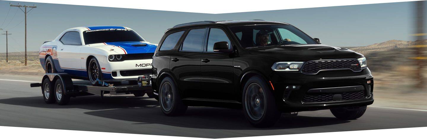 The 2022 Dodge Durango equipped with a 5.7L V8 towing a race car on a flatbed.