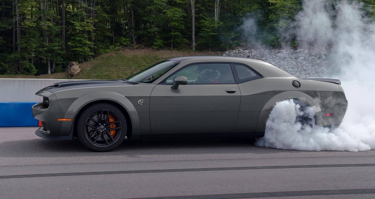 Display A driver-side profile of a gray 2023 Dodge Challenger R/T Scat Pack Widebody with the Swinger Special Edition Appearance Package on a track with smoke billowing from its rear tires.