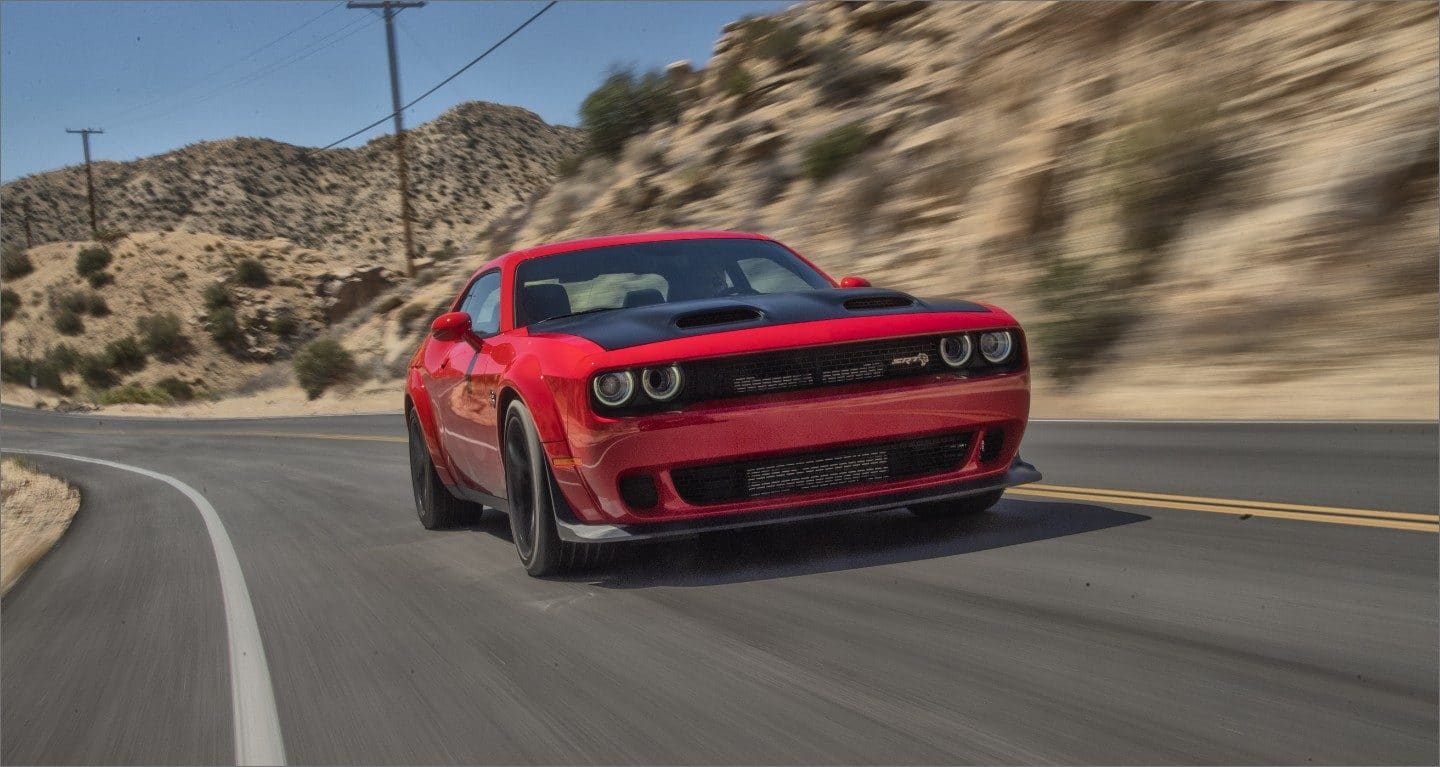 Display A red 2023 Dodge Challenger SRT Jailbreak being driven on a curved highway with the background blurred to indicate the speed of the vehicle.