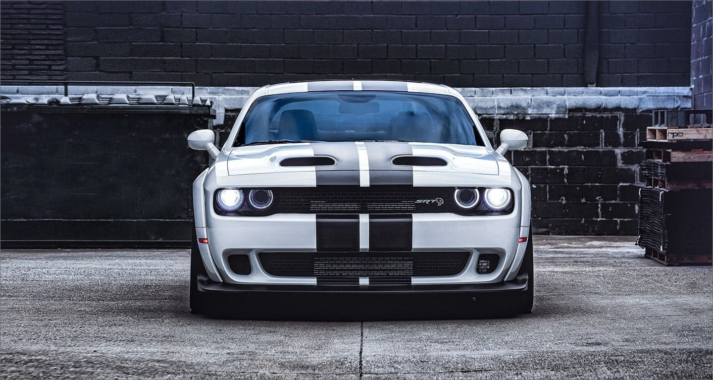 Display A white 2023 Dodge Challenger SRT Hellcat with black center stripes, parked in an alley.