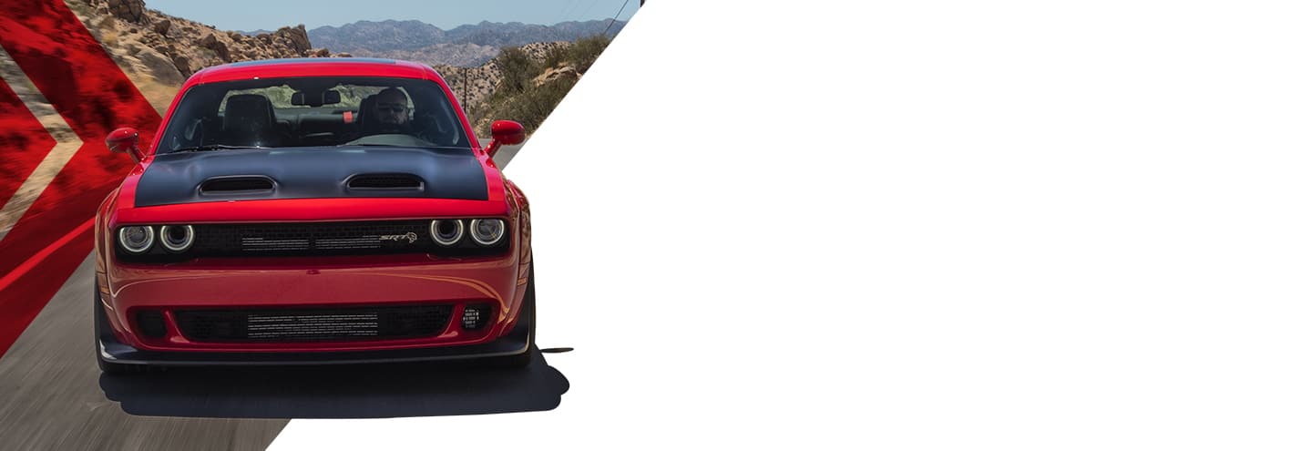 A front angle of a red 2023 Dodge Challenger SRT Hellcat with a black hood, being driven on a highway through the mountains.