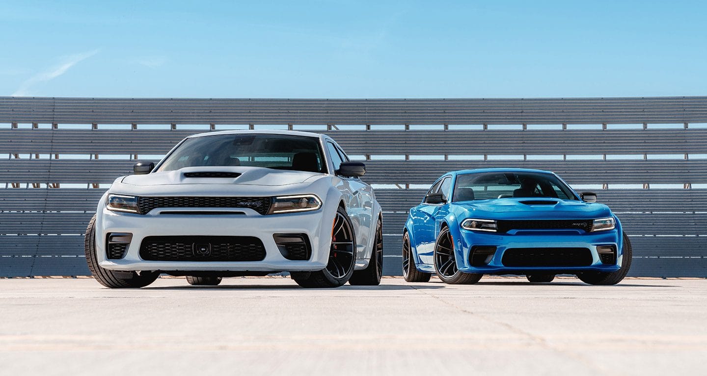 Display Two Dodge Charger models parked at a track. On the left: a white 2023 Dodge Charger SRT Hellcat. On the right: a blue 2023 Dodge Charger SRT Hellcat.