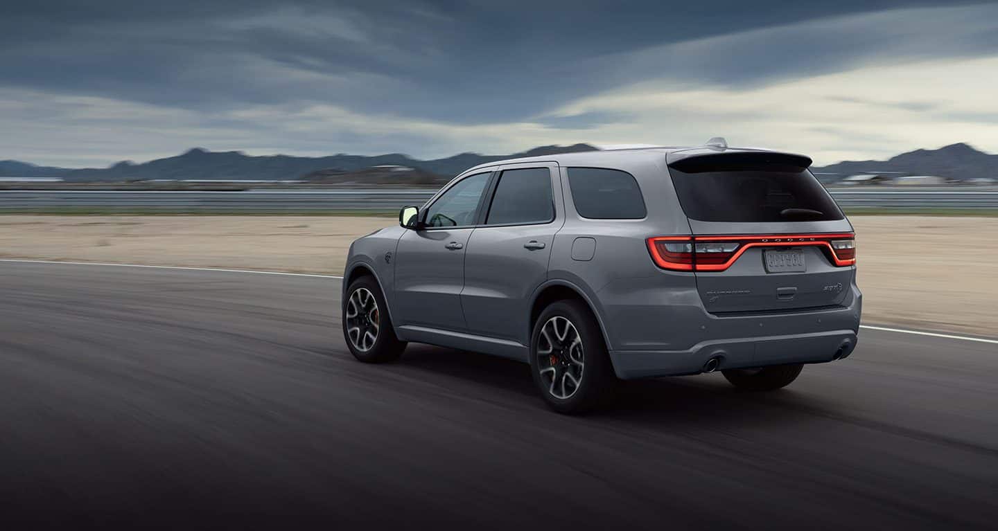 Display A three-quarter rear view of the 2023 Dodge Durango R/T being driven on a track at dusk, its taillamps lit.