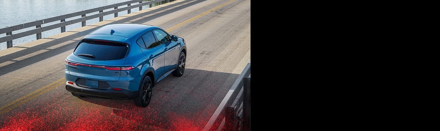 A rear view of a 2023 Dodge Hornet R/T with the available Blacktop Package, being driven across a bridge over water.
