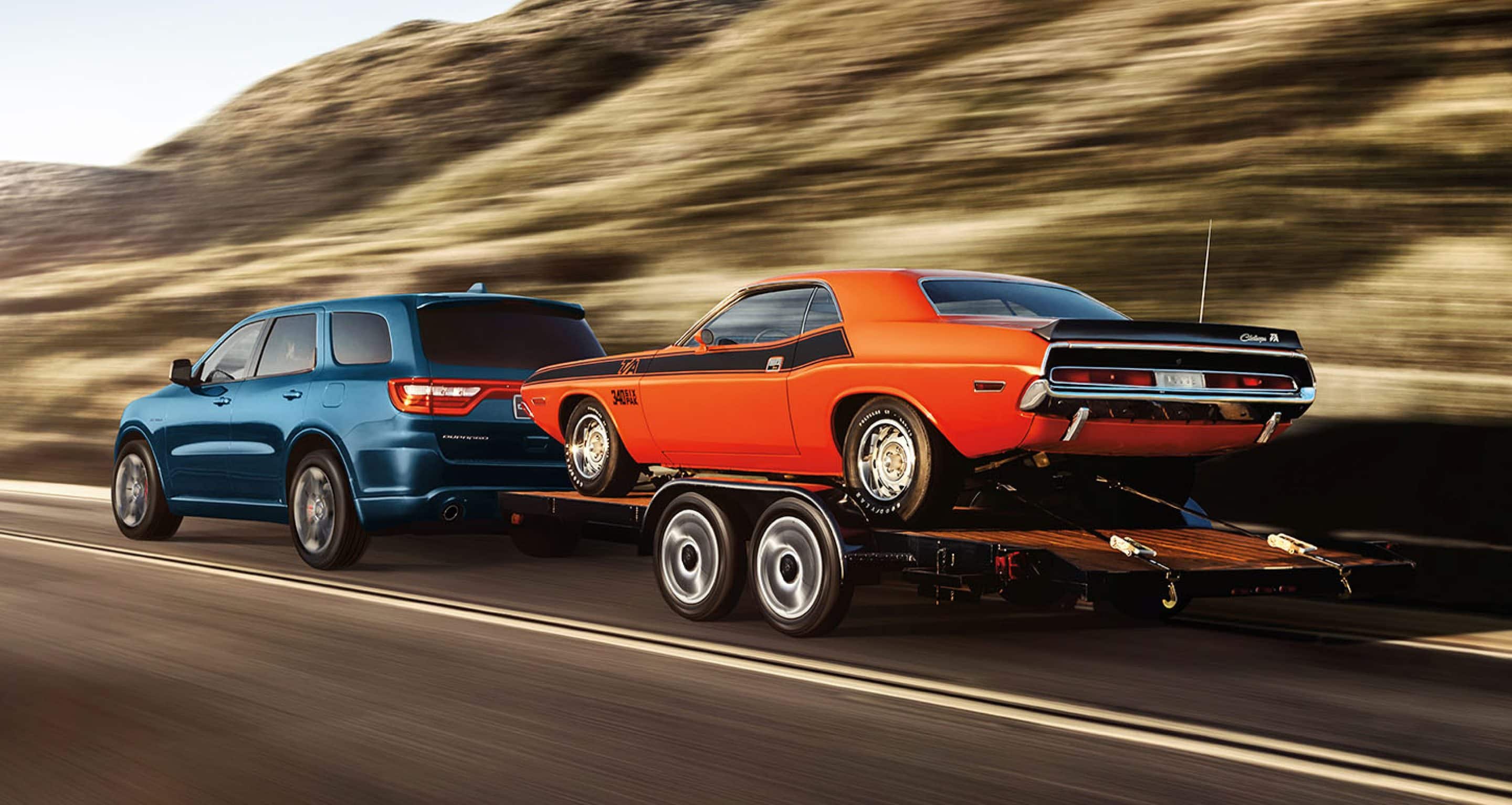 2024 dodge durango towing orange muscle car on highway. 