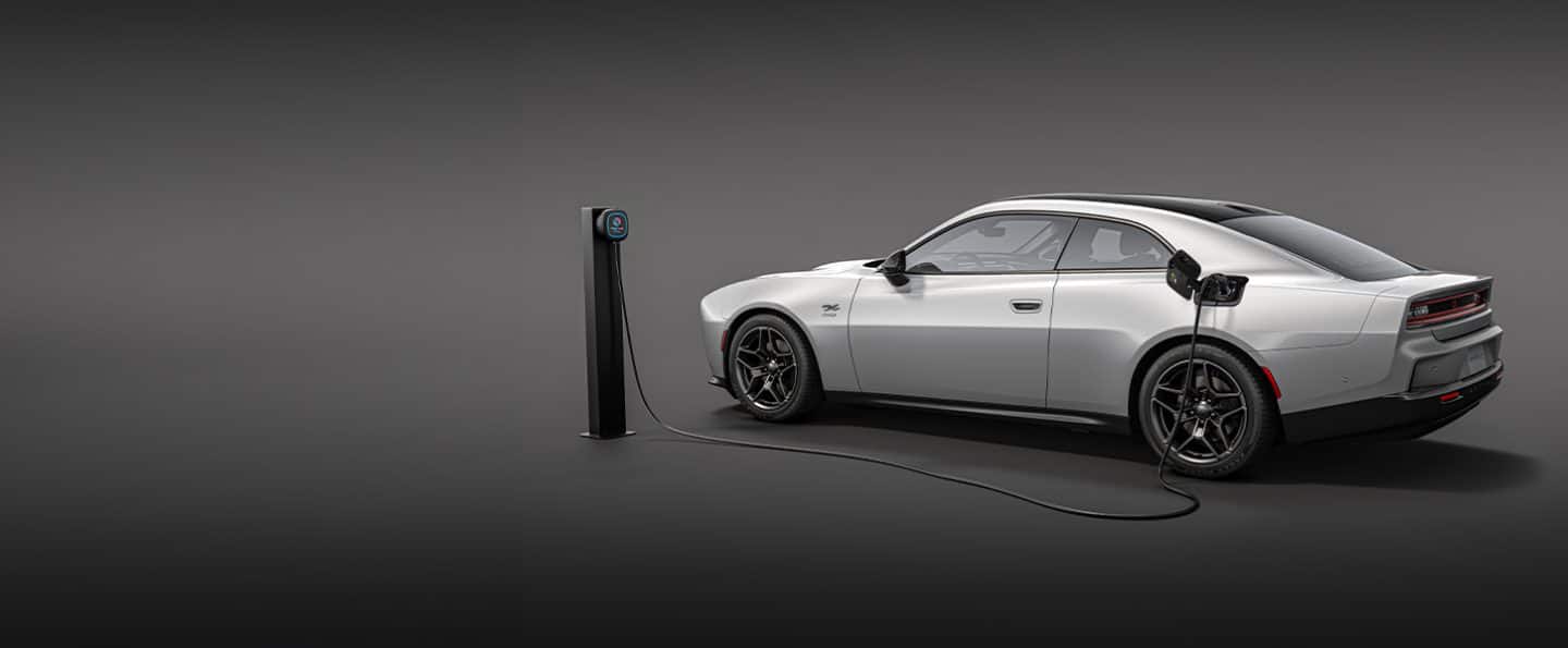 A silver 2024 Next-Gen Charger Daytona BEV two-door with a Level 2 charging station's charging cord plugged into the vehicle's charging port.