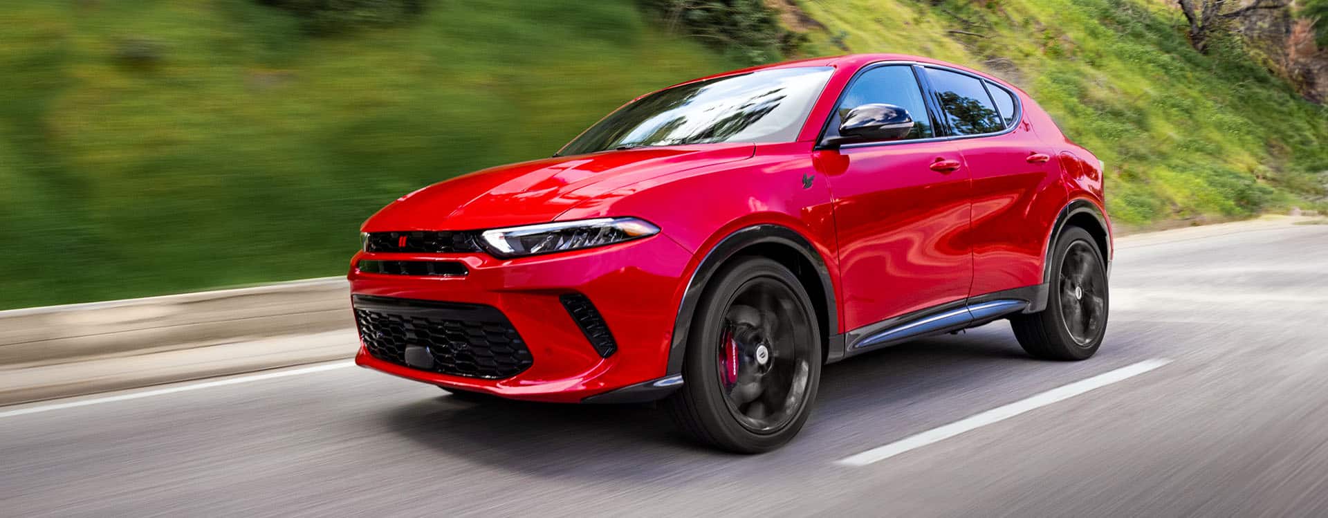 A red 2025 Dodge Hornet R/T PHEV traveling on a highway with the background blurred.