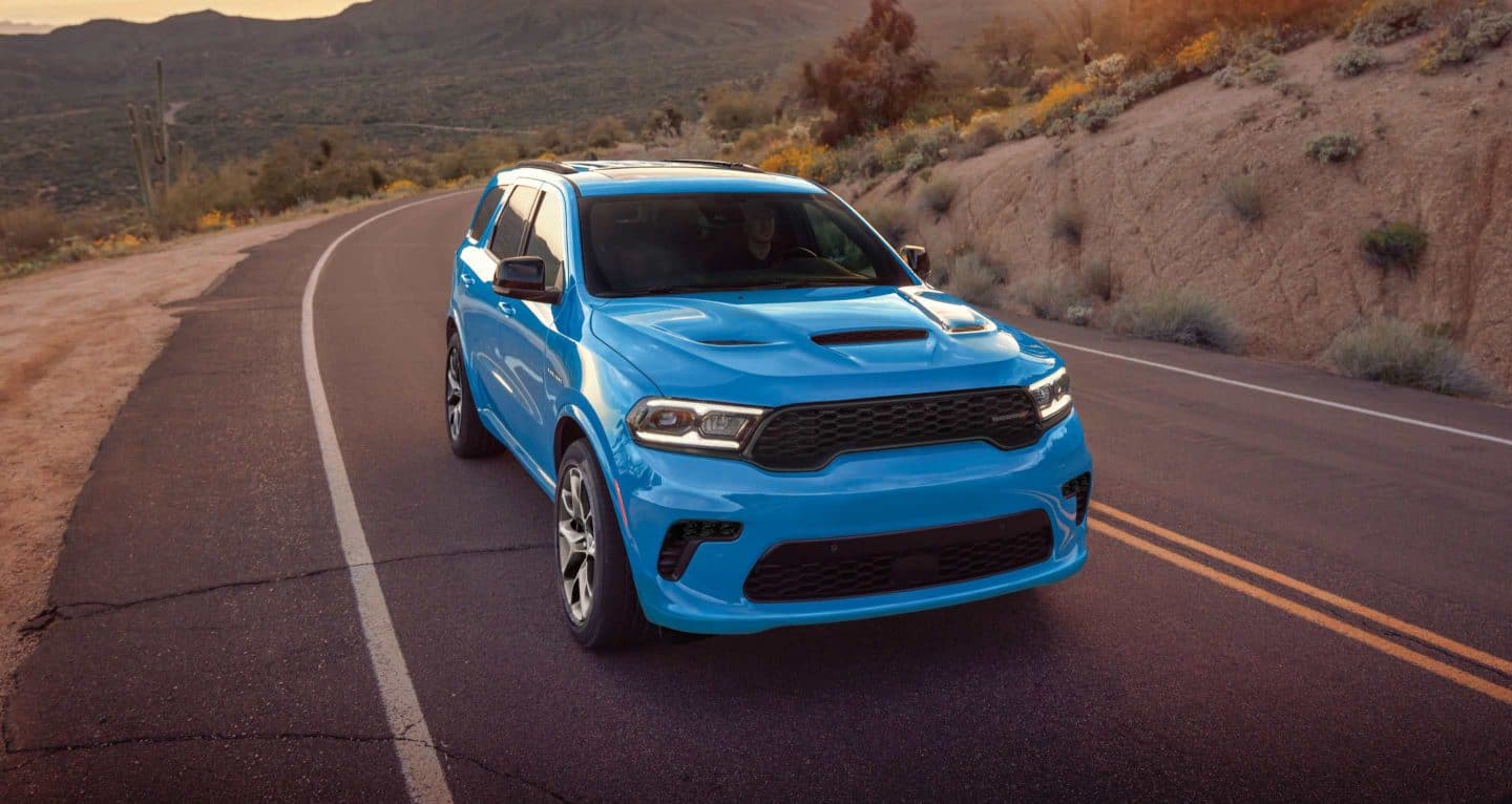 Display A blue 2026 Dodge Durango GT HEMI traveling down a winding highway in the mountains.