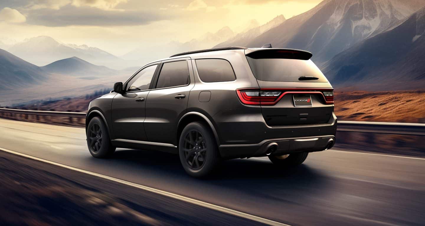 Display A driver-side rear angle of a gray 2026 Dodge Durango GT HEMI traveling down a highway at sunset.