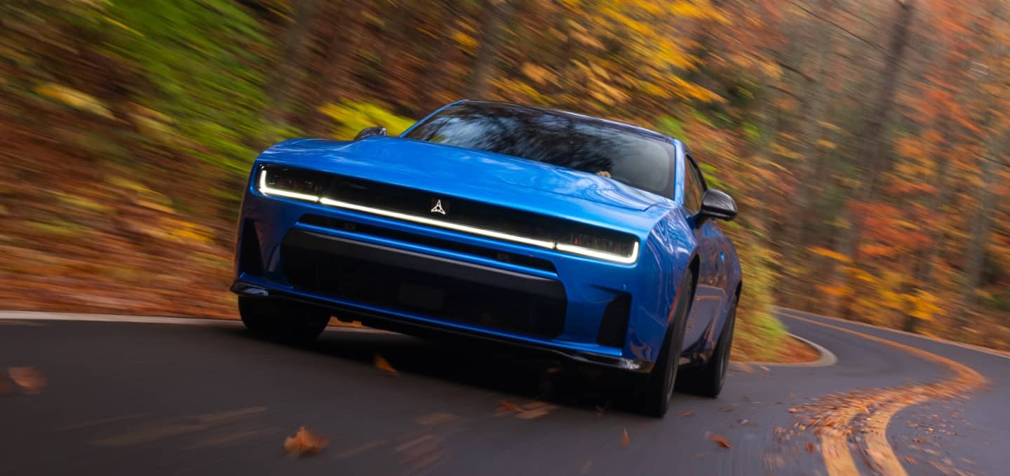 A blue 2027 Dodge Charger Scat Pack taking a curve on a country road.