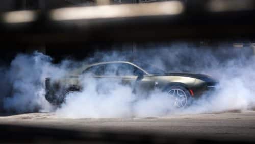 A silver 2027 Dodge Charger Scat Pack in profile, with smoke surrounding the car.
