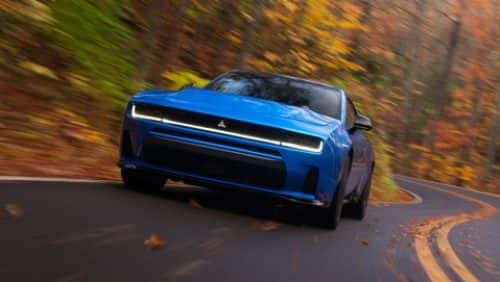 A blue 2027 Dodge Charger Scat Pack taking a curve on a country road.