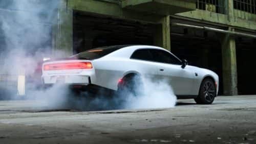 A white 2027 Dodge Charger Scat Pack, with smoke coming from its rear tires, shot from a rear profile.