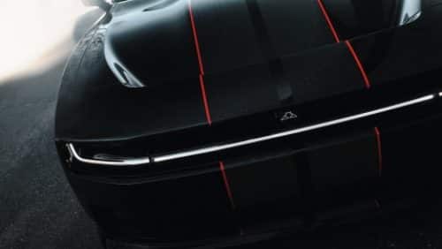 The hood and front end of a black  2027 Dodge Charger Scat Pack with dual black and red center stripes.