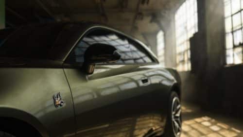 The driver's side of an olive green 2027 Dodge Charger Scat Pack, parked in an industrial garage.