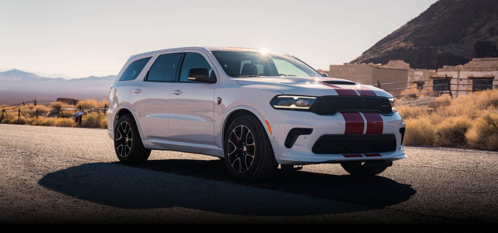 A white 2027 Dodge Durango SRT Hellcat Jailbreak with dual red center stripes parked on a highway in the desert. Pure Swagger.