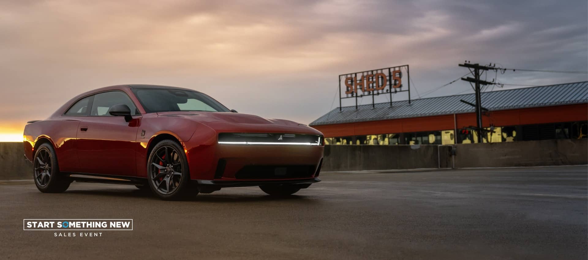 A passenger-side front angle of a red 2025 Dodge Charger Daytona Scat Pack at dusk. The Start Something New Sales Event.