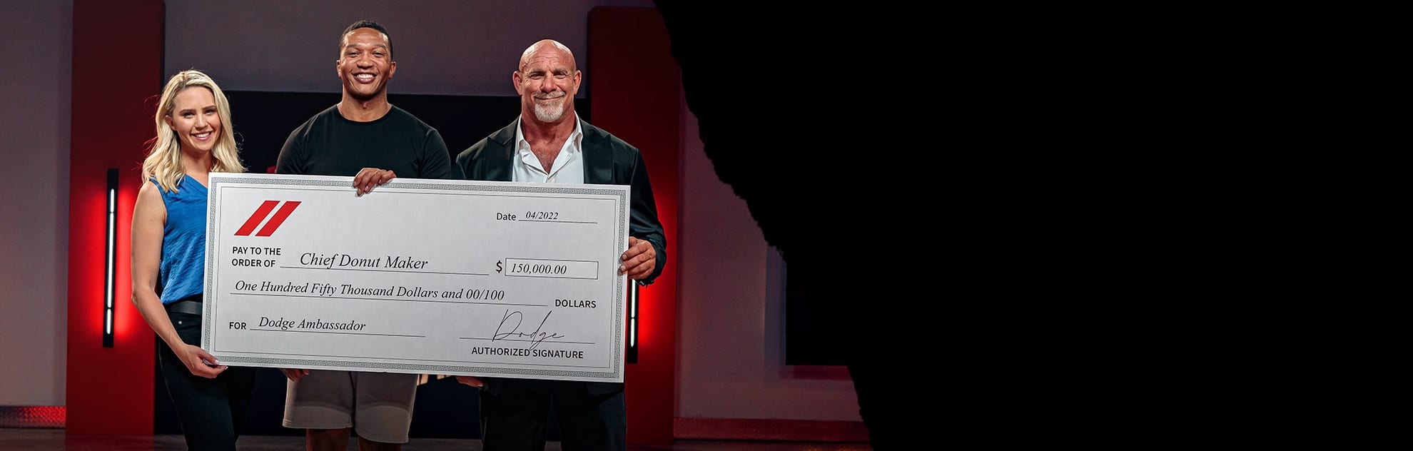 Katie Osborne—Dodge Host, Preston Patterson—Chief Donut Maker Winner and Bill Goldberg—Championship Wrestler, all smiling, holding a jumbo check for $150,000 made payable to the Chief Donut Maker and signed by Dodge.