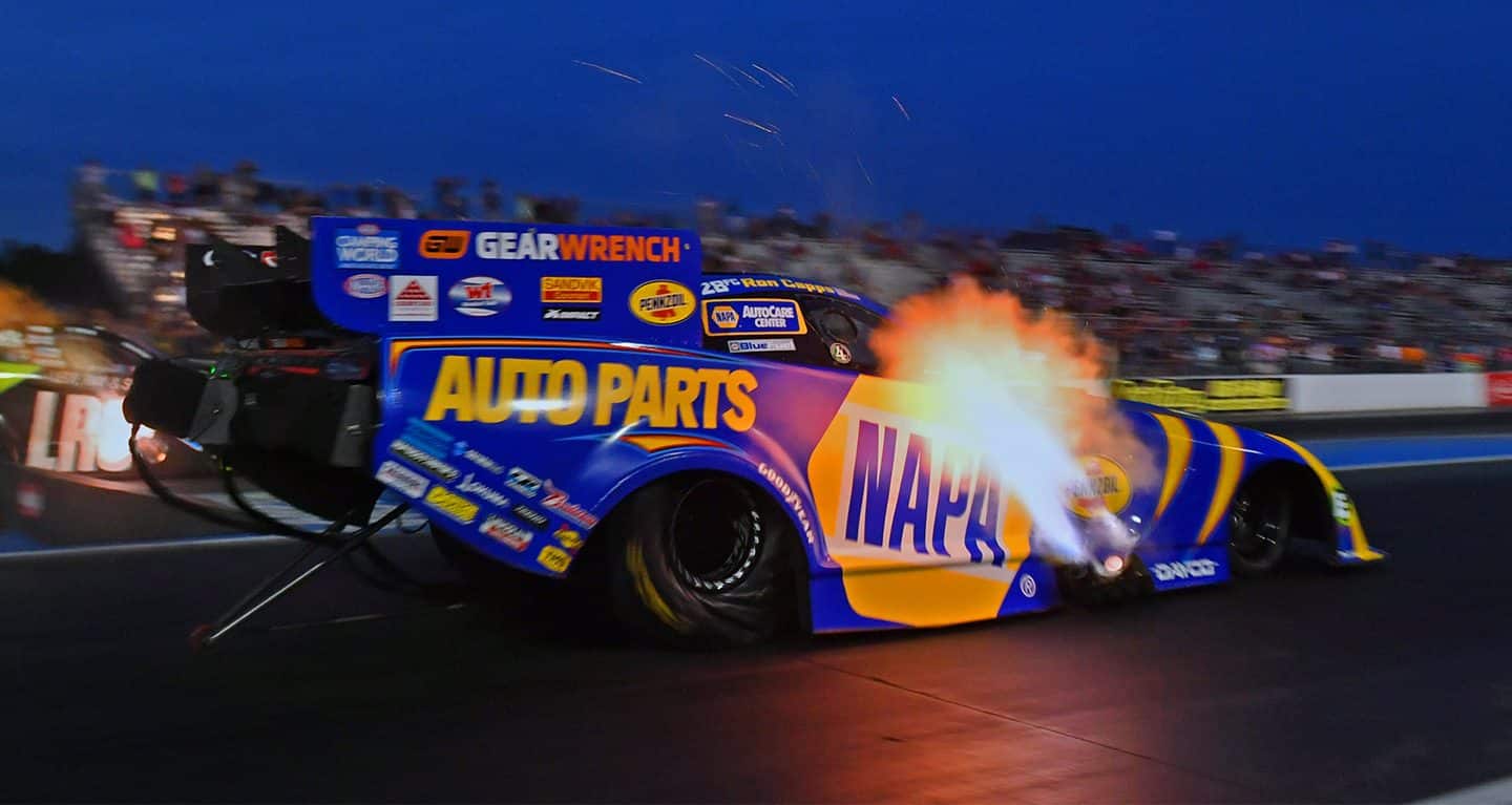Display A blue and yellow funny car photographed at dusk with flames coming from the exhaust pipes on the side of the vehicle.