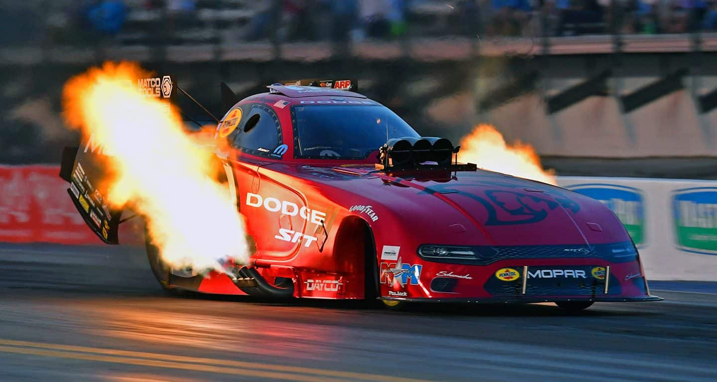 Display A red funny car photographed at night with flames coming from the exhaust pipes on either side of the racecar.