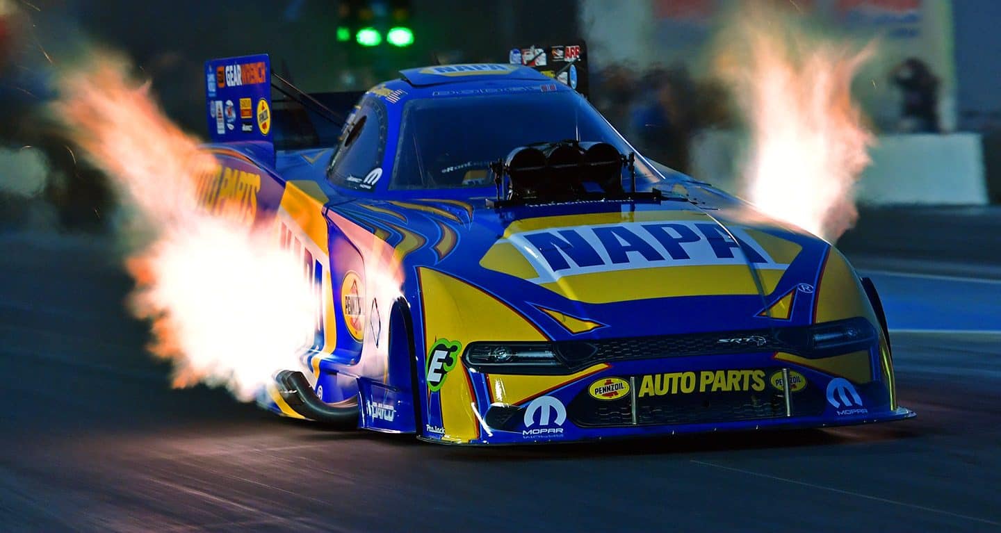 Display A three-quarter profile of a blue and yellow funny car with flames coming from the exhaust pipes on either side.
