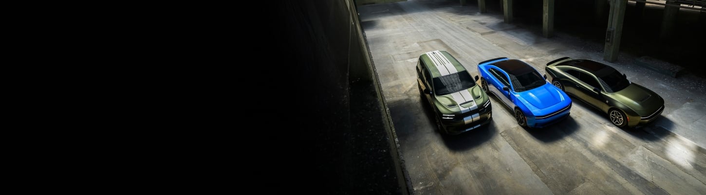 An overhead angle of a green 2026 Dodge Durango SRT Hellcat Jailbreak with dual white center stripes, a blue 2026 Dodge Charger Scat Pack with black roof and a green 2026 Dodge Charger Scat Pack Plus parked near each other.