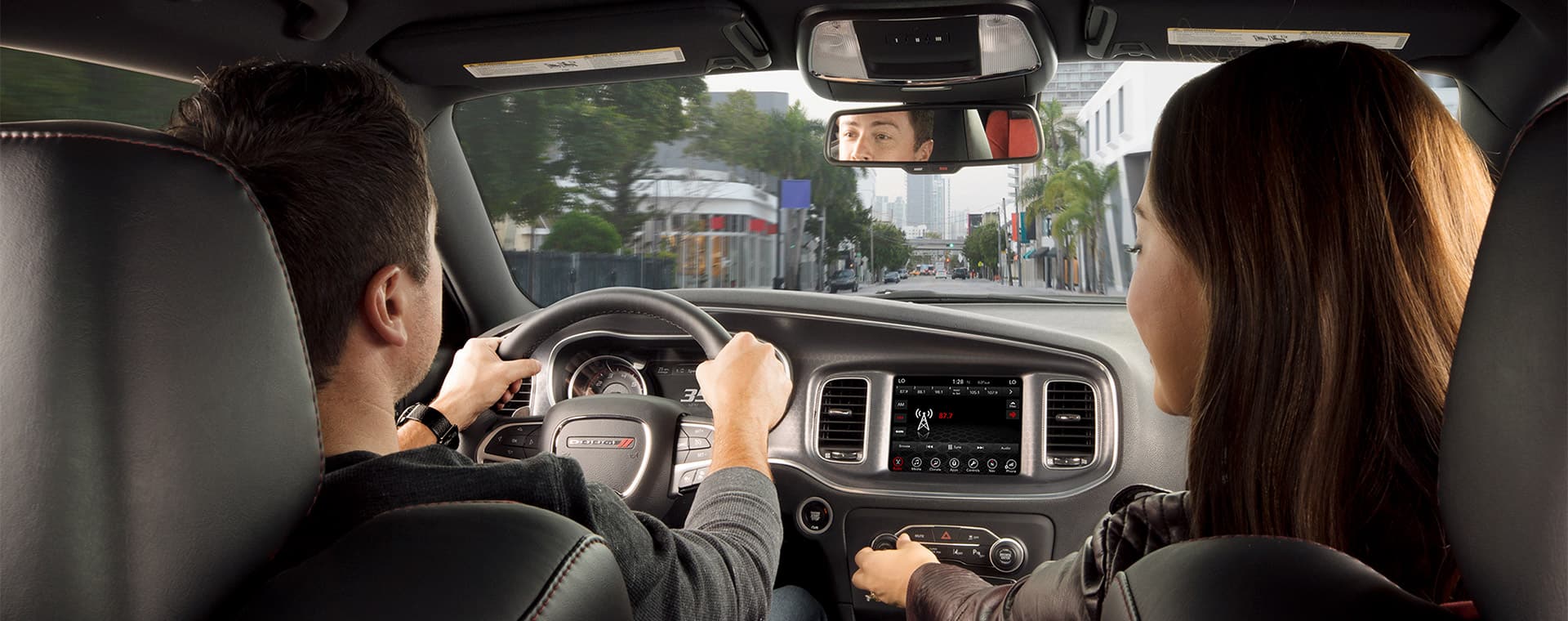 An interior view of a 2021 Dodge Charger with the driver focusing on the road ahead and the front passenger adjusting the climate controls.