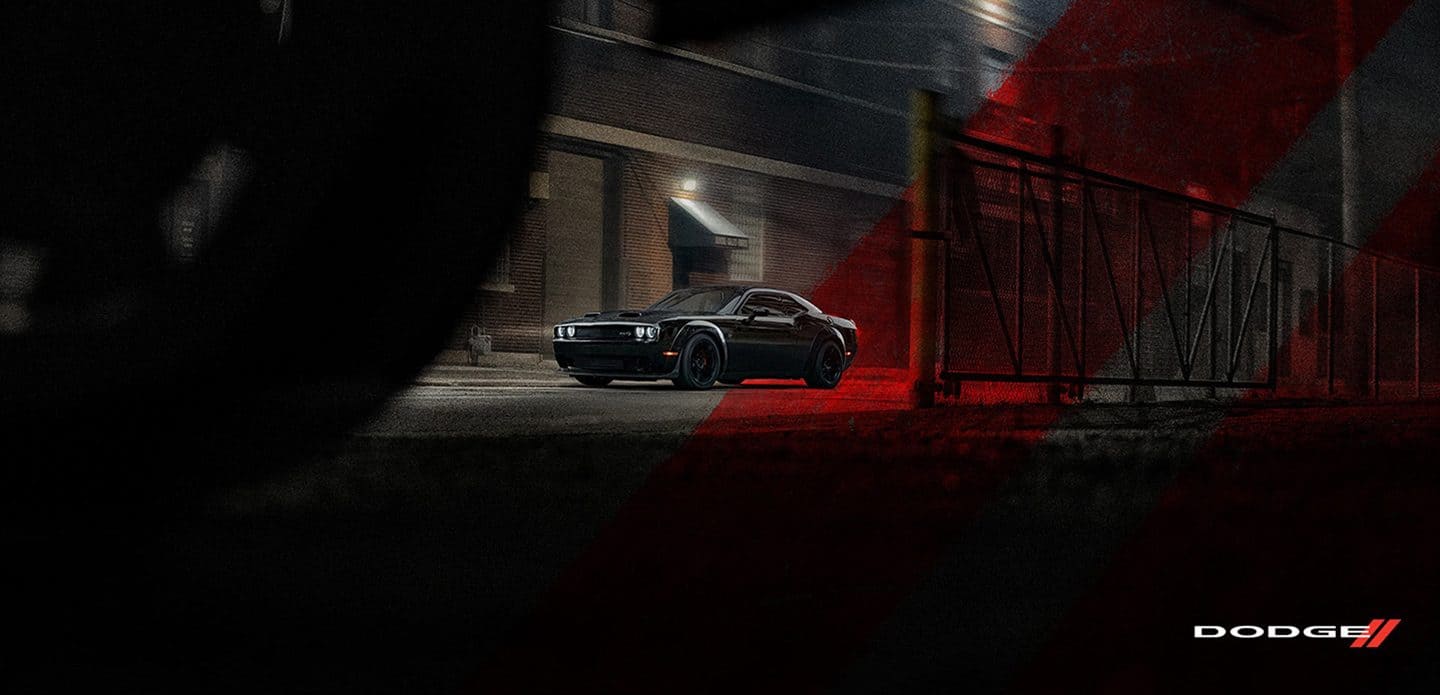 Display A black 2021 Dodge Challenger SRT Hellcat Widebody parked in an alley, at night, with the red Dodge racing stripes superimposed across the background.