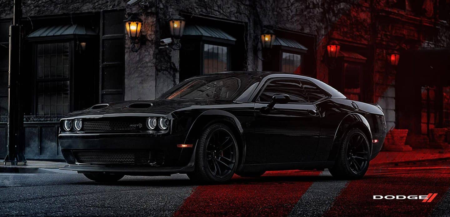 Display A black 2021 Dodge Challenger SRT Hellcat Widebody parked at a classically-designed building, at night, with the red Dodge racing stripes superimposed across the background.